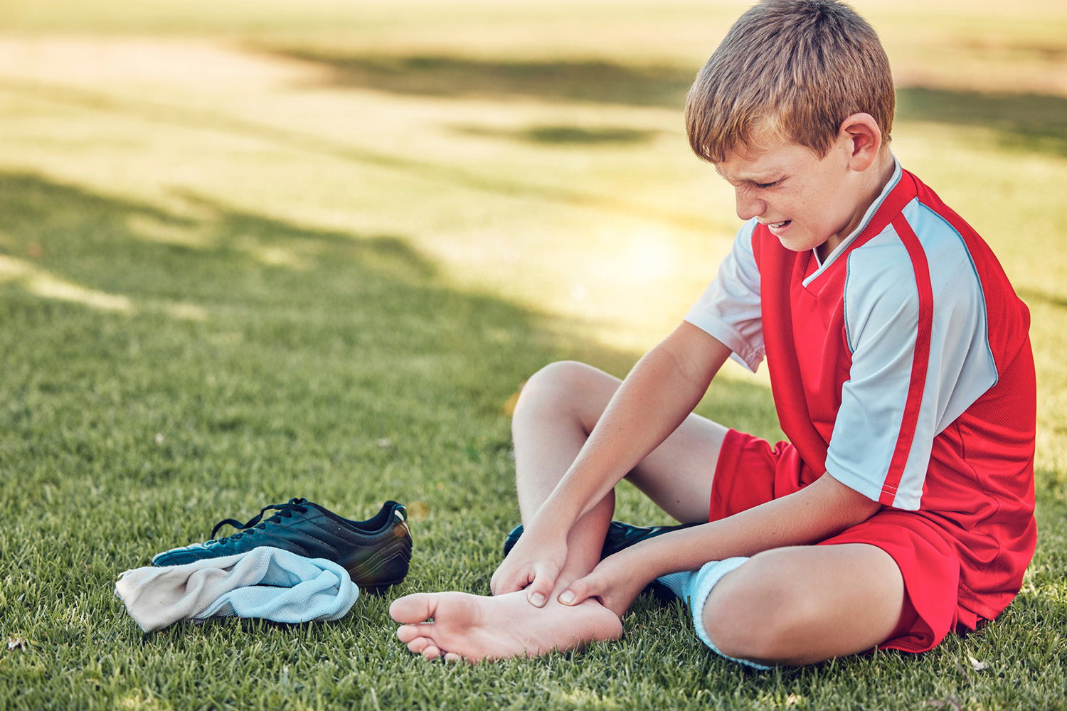 Child athlete sitting on ground holding his heel in pain